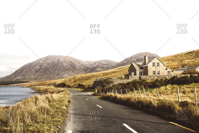 Peaceful beautiful landscape including lonely road and house on the background of mountains