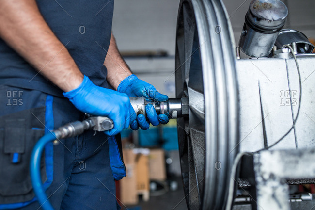 Close-up of a mechanic using an air impact wrench to detach a flywheel from a compressor engine