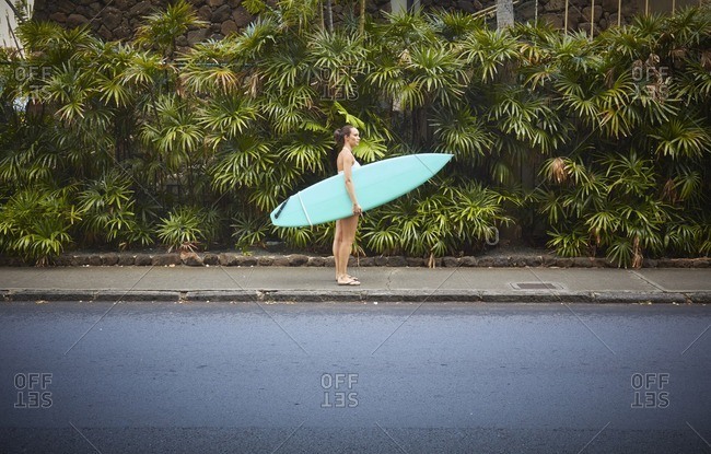 Pacific Islander woman standing on sidewalk holding surfboard