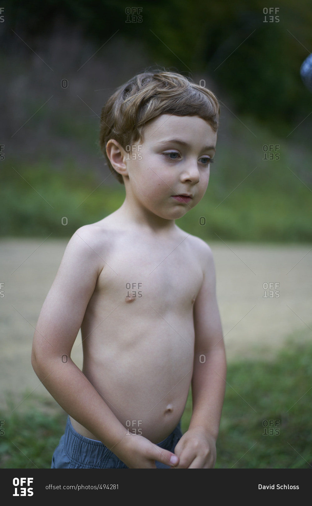 Boy in jeans and no shirt standing beside a dirt road stock photo - OFFSET