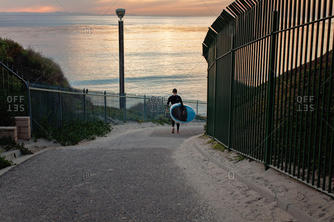 Surfer carrying surfboard down a path toward the ocean
