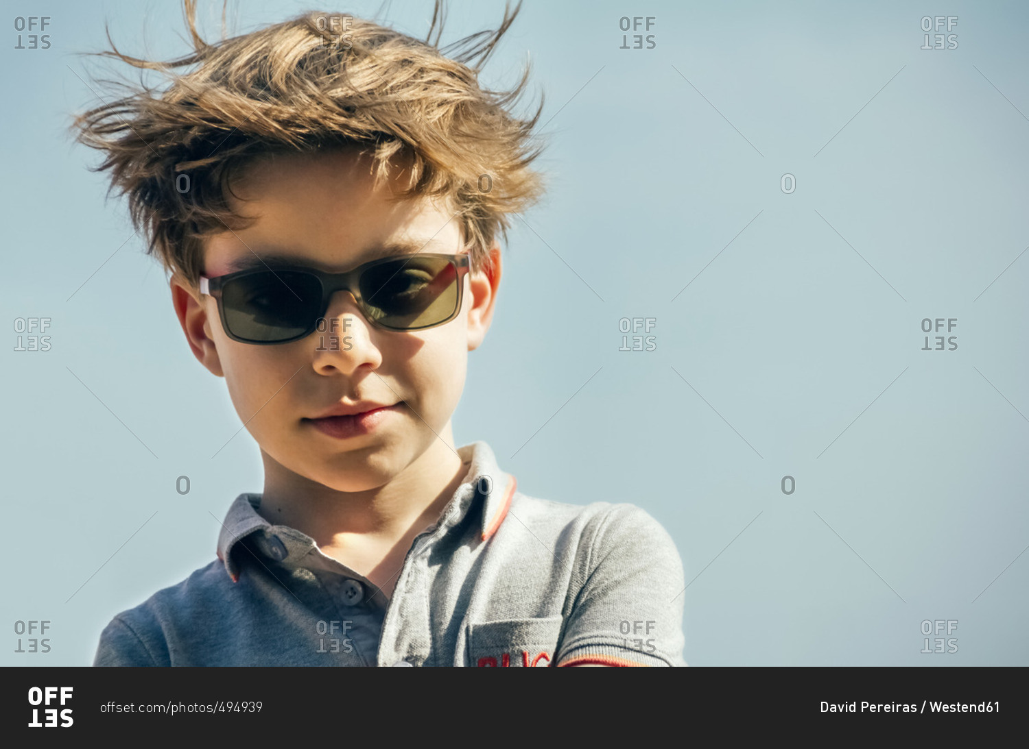 Portrait of cool boy with sunglasses and blowing hair in front of sky