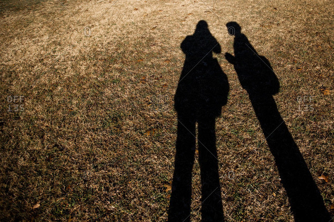 Long Shadow Of Mother And Son Standing Together On Lawn Stock