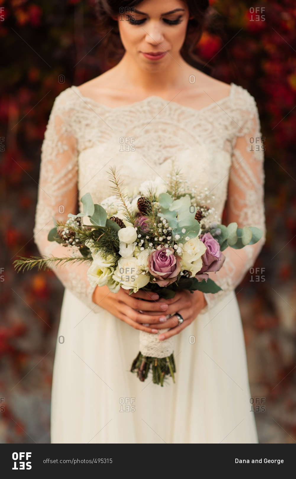 Close up of a bride holding bouquet standing by colorful fall vines