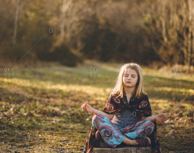 Little girl sitting on a tree stump meditating