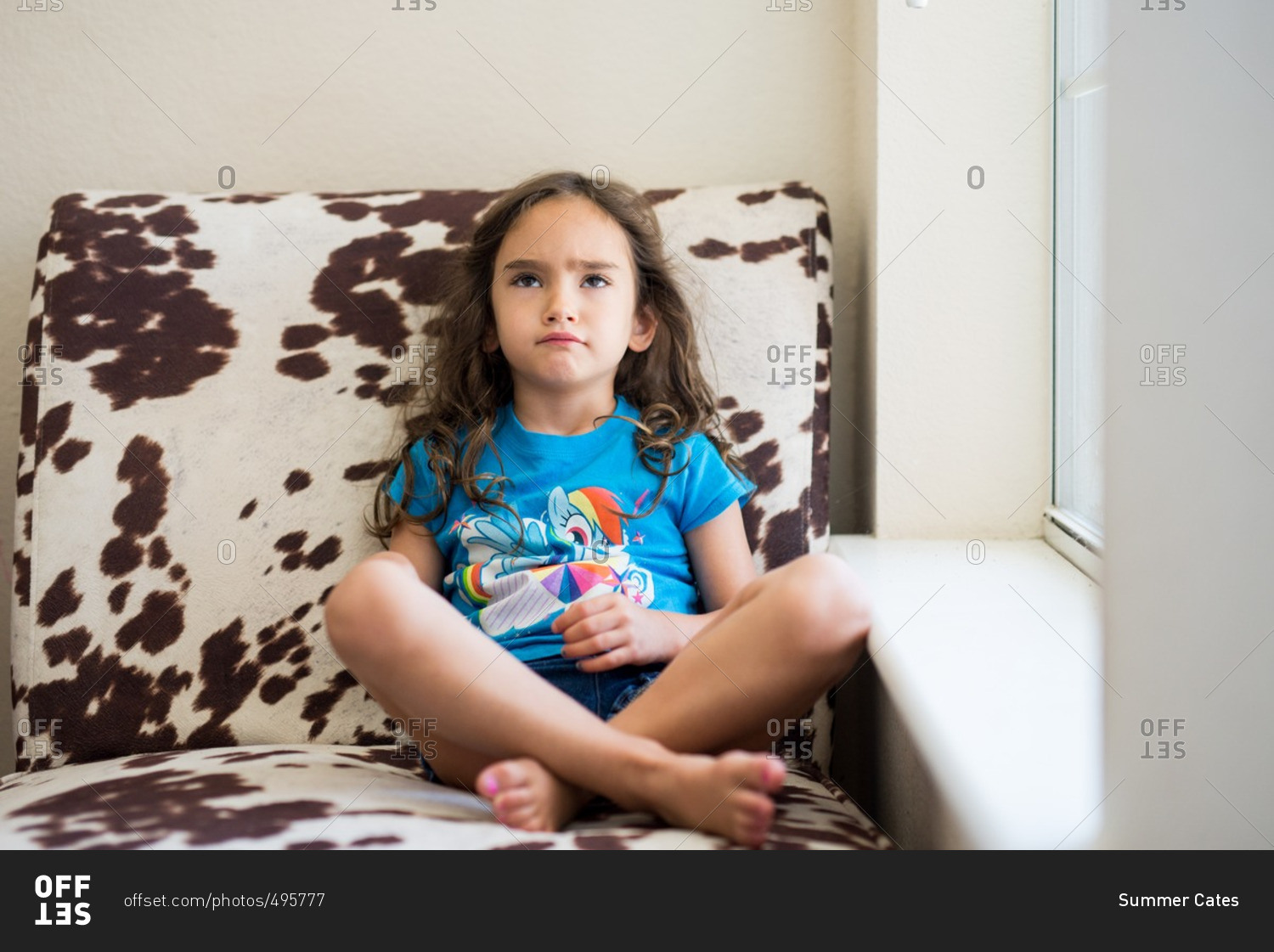 Little girl pouting while sitting in a cow print chair