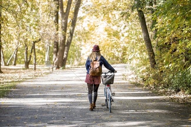Rear view of woman with bicycle walking on road amidst trees