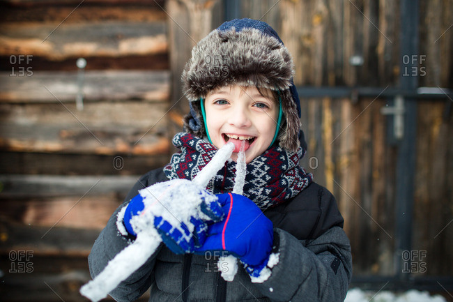 Smiling child sticking out a tongue and tasting icicles with wooden cabin door in the background