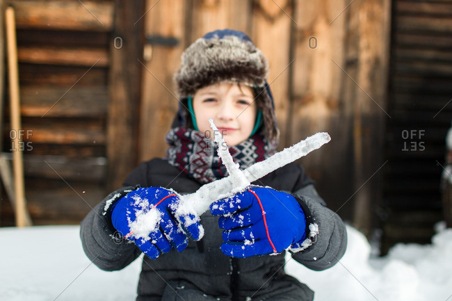 Child in front of a wooden wall playing in a snowy garden with focus on gloves and crossed icicles