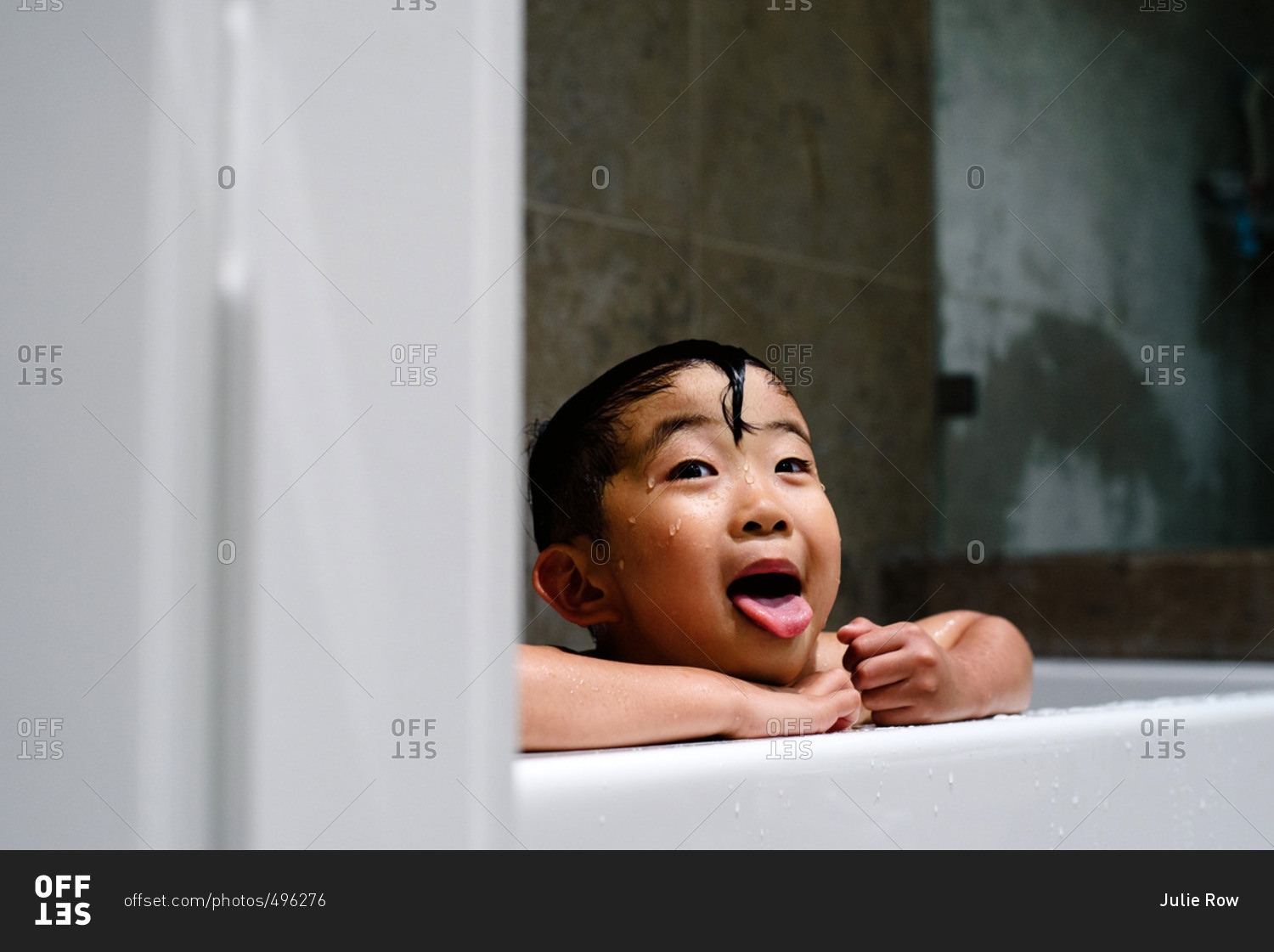 Little boy with head above bathtub sticking out tongue stock photo