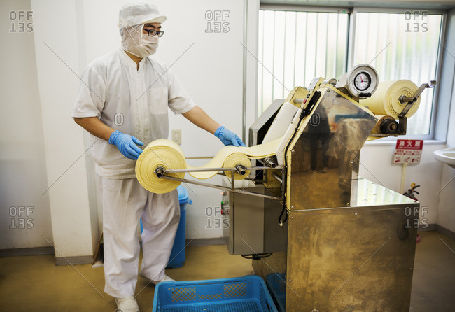 A Soba noodle factory.  Sheets of fresh noodle dough being passed through a large pressing machine.