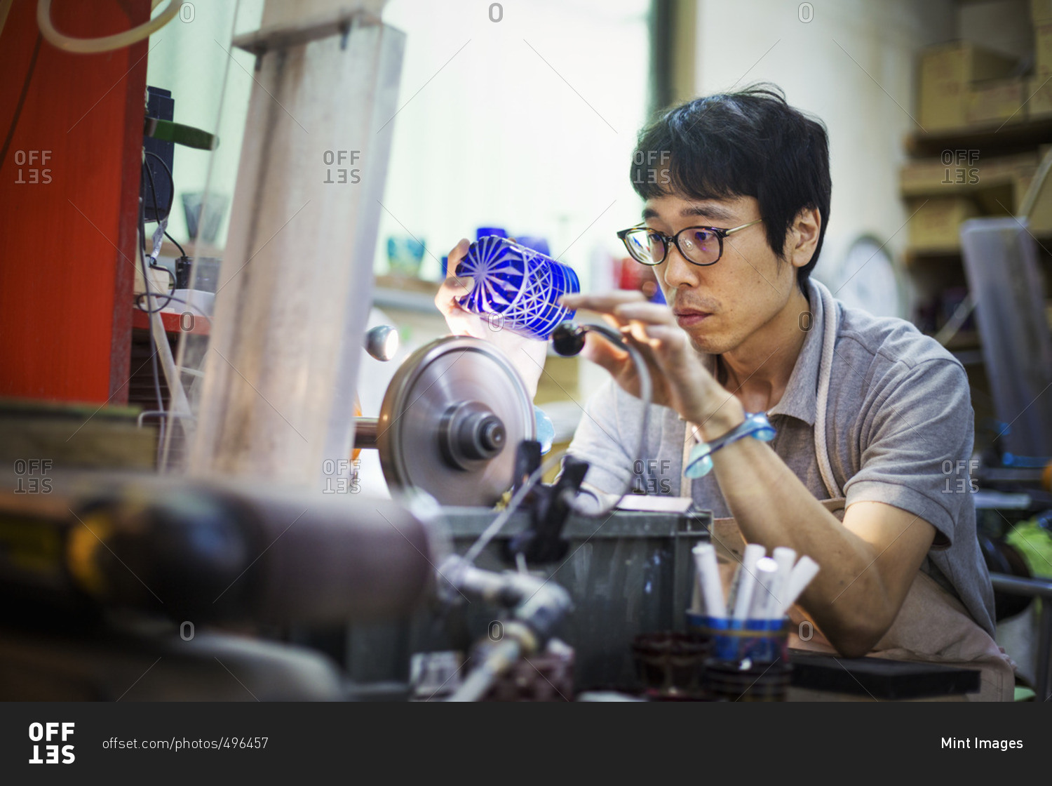 A craftsman at work in a glass maker\'s workshop polishing a vivid blue cut glass object.
