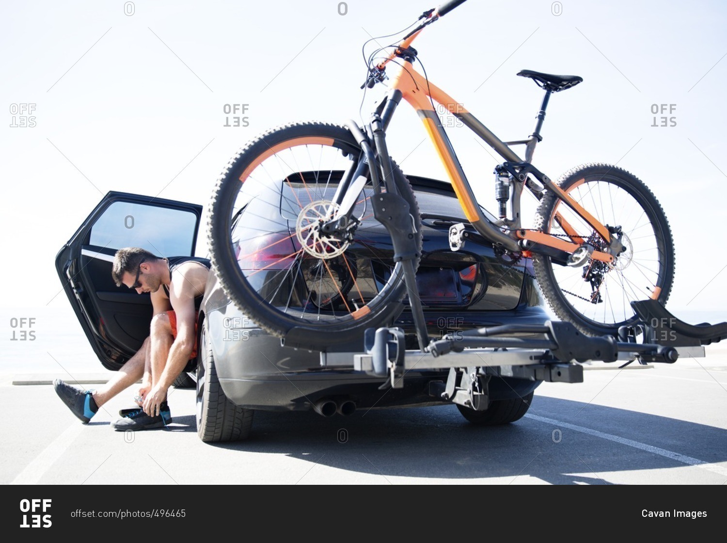 Man tying shoelace while sitting in car with bicycle