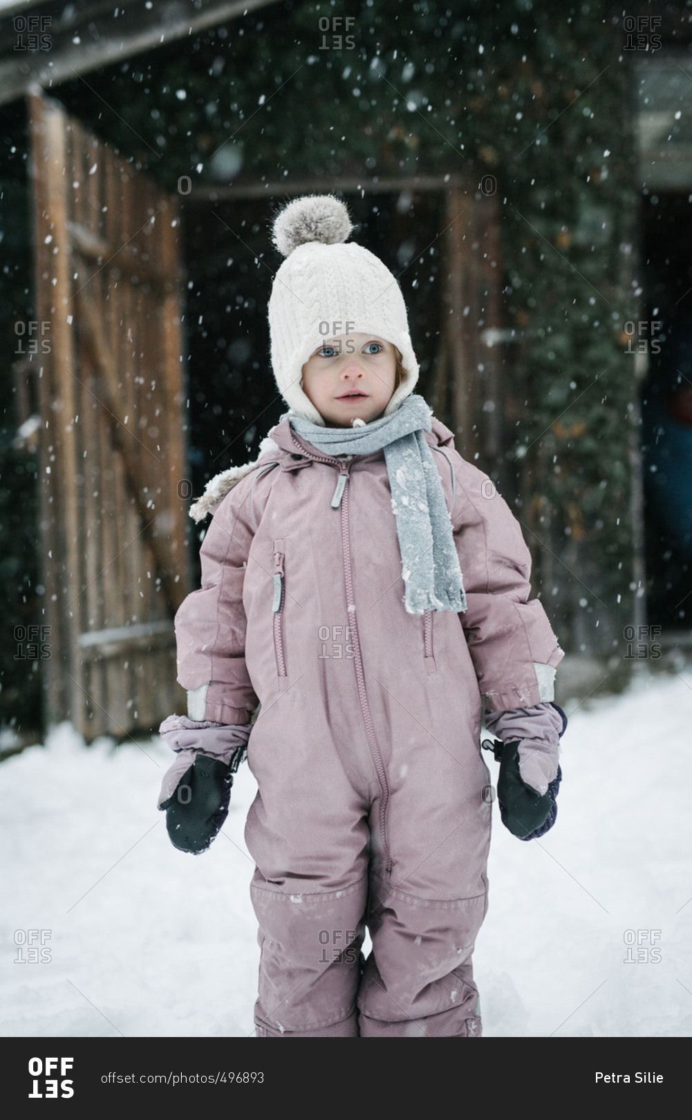 Portrait of toddler girl in a pink snowsuit during a snow storm stock