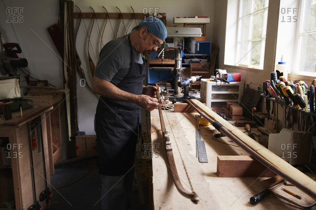 A bow maker working on a wooden bow in his workshop.