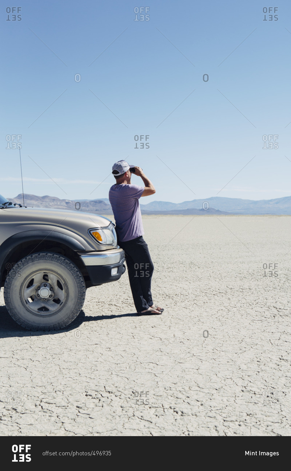 Man standing on vast desert, looking through binoculars and leaning against truck, Black Rock Desert