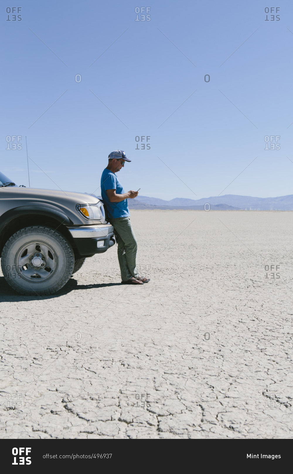 Man leaving against truck in desert, using smart phone, Black Rock Desert, Nevada
