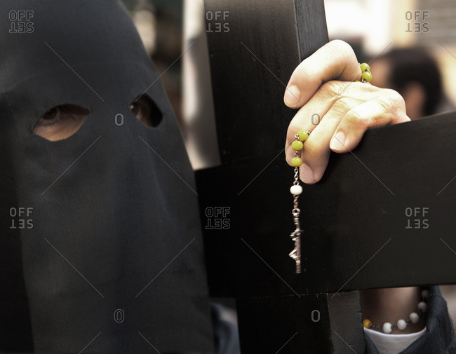 Person in a hooded robe carrying a cross during an Easter procession in Seville, Spain