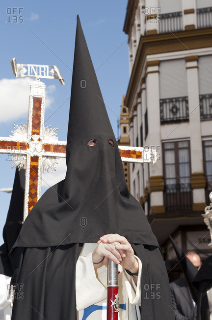 Person in a hooded robe standing in a street during an Easter procession in Seville, Spain