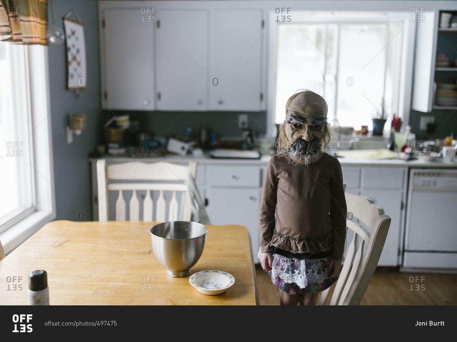Little girl in an old man mask standing in a kitchen chair