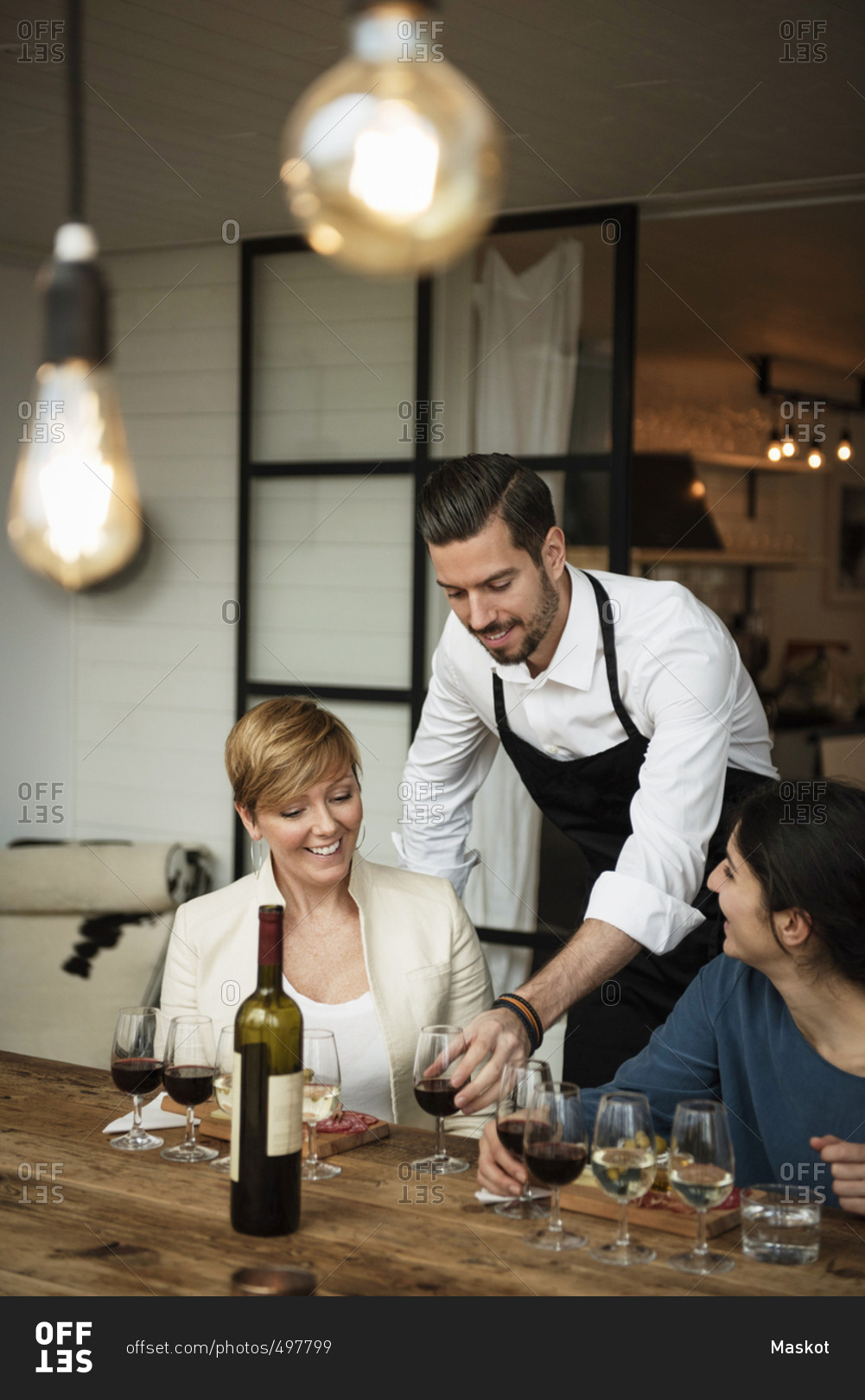 Smiling man wearing apron serving wine to businesswomen at table