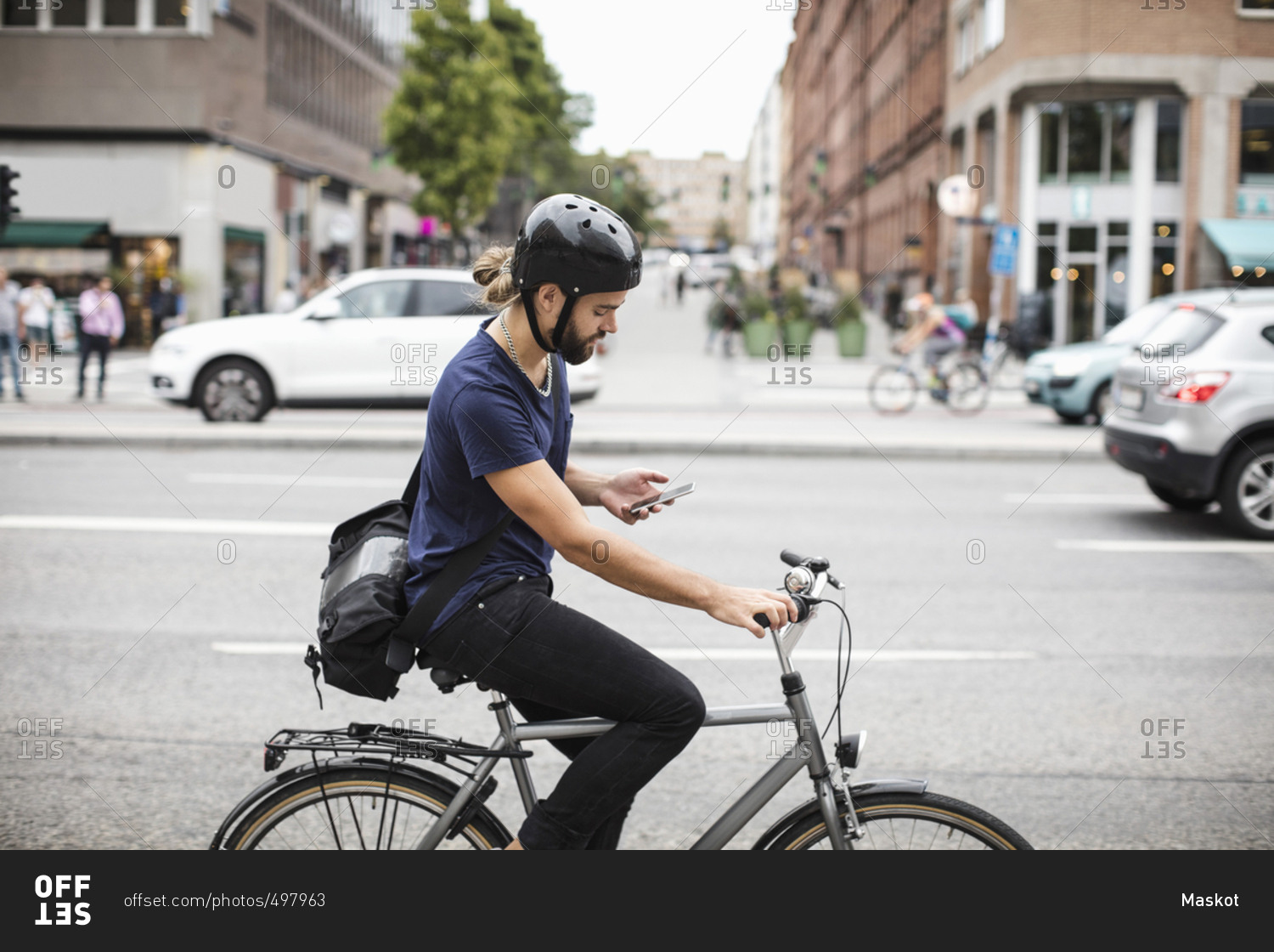 Side view of man using mobile phone while riding bicycle on city street