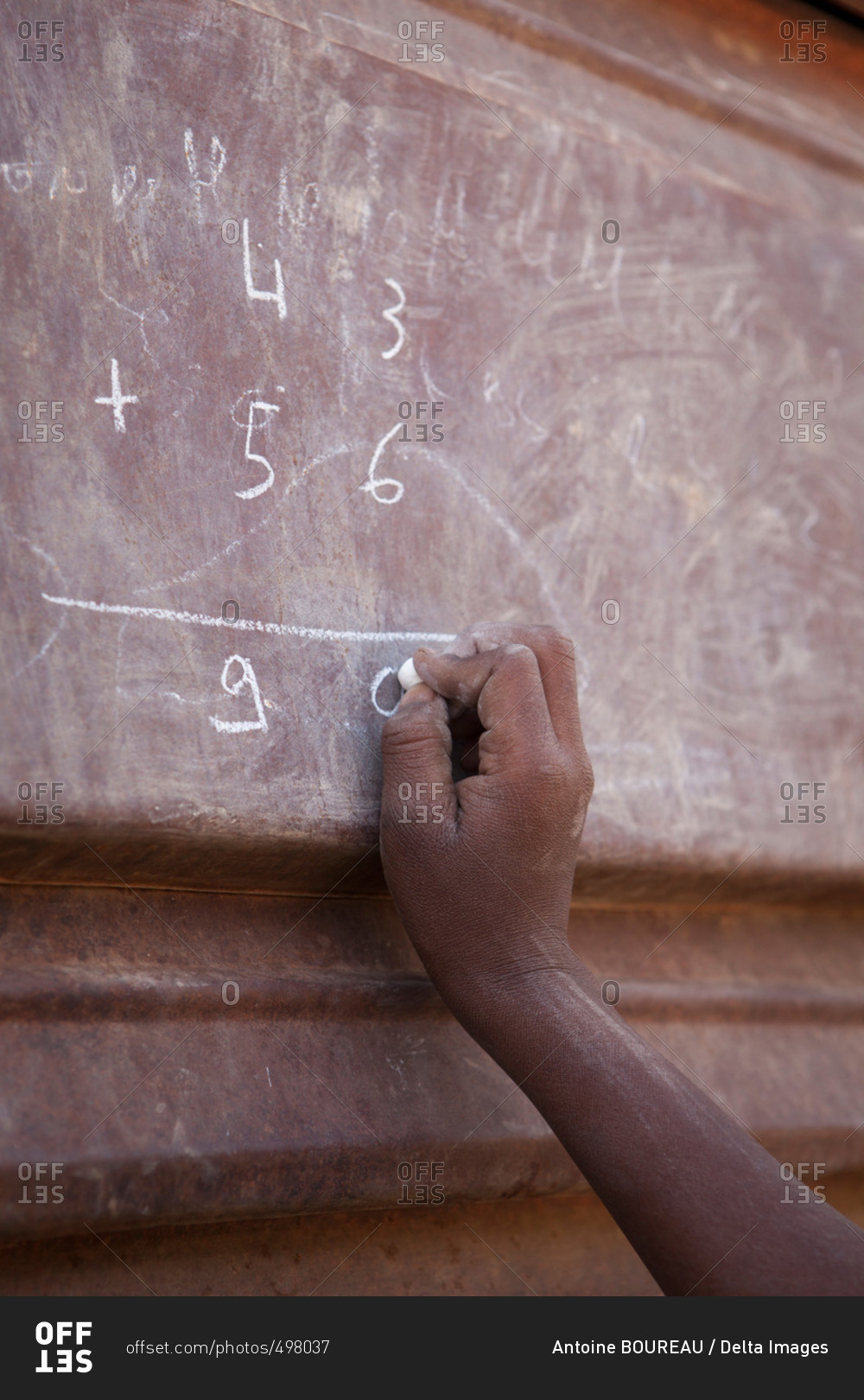 Burkina Faso, Ouagadougou area, Girl revising her math lessons with a chalk on a metallic door