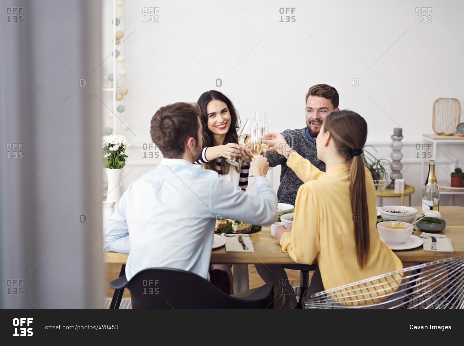 Happy friends toasting champagne flutes while sitting at dinning table in lunch party