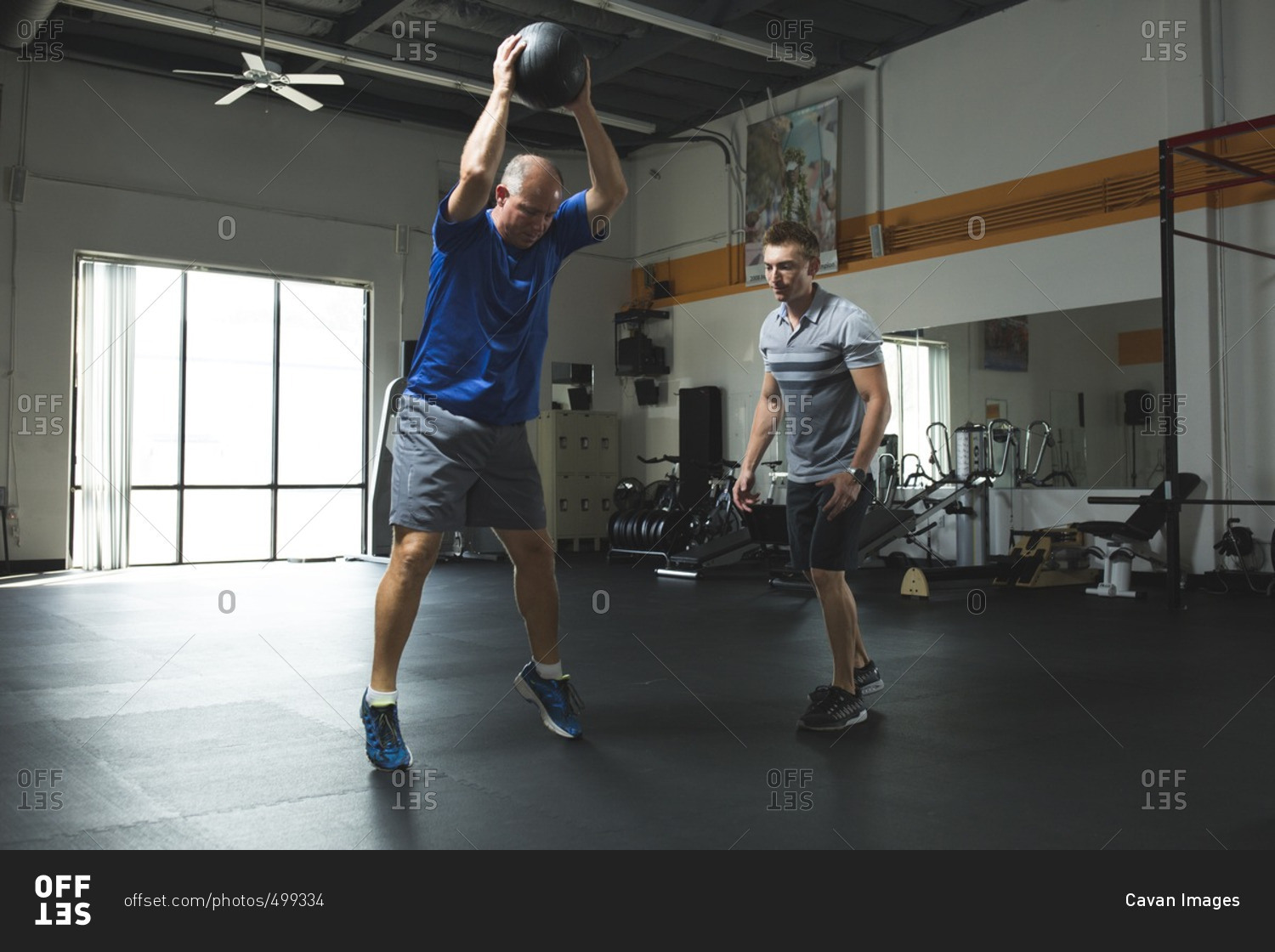 Trainer looking at customer exercising with fitness ball in gym