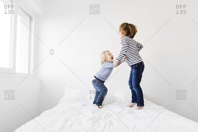 Happy siblings jumping on bed against wall at home