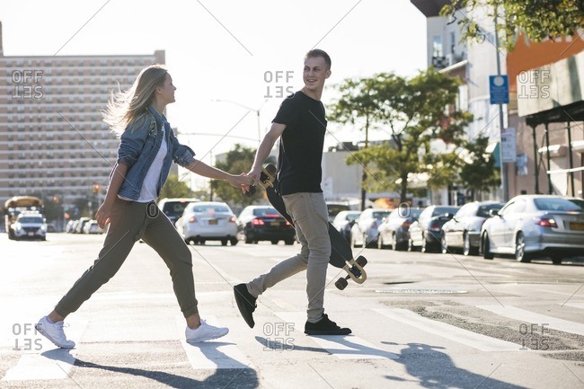 Man holding skateboard walking with girlfriend on city street