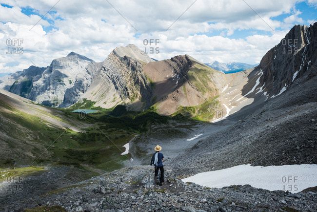 Man looks out over expansive mountains, lake, forest in summer