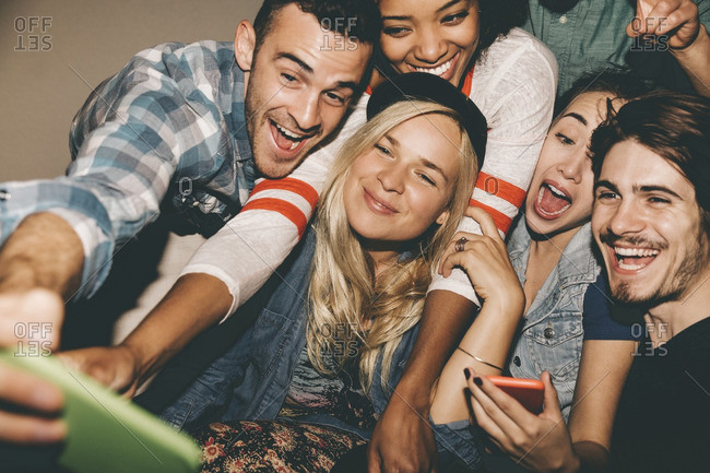 Multiethnic friends taking selfie through smart phone during house party