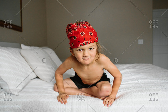 Little boy wearing red bandana on a bed leaning forward