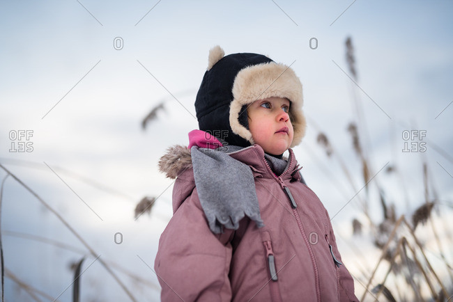 Portrait of a toddler girl wearing an anorak and hood outside in nature in the winter