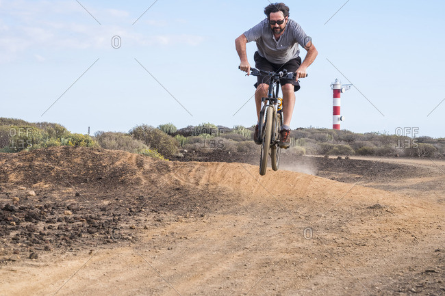 Man riding bike off jump on dirt trail in desert