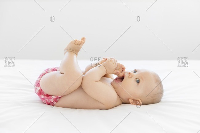 Baby girl lying on bed trying to put her foot in mouth