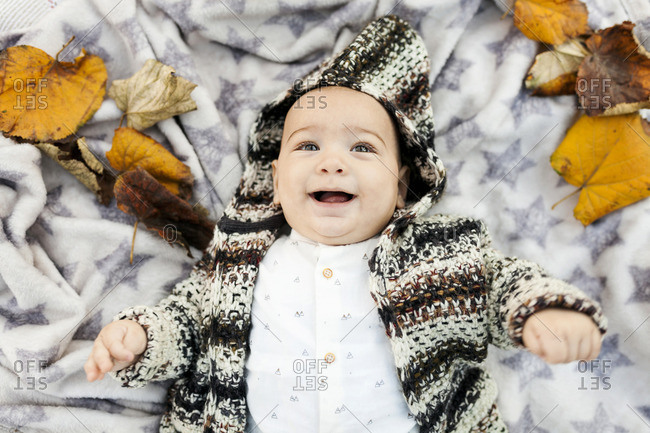 Happy baby boy lying on a blanket with autumn leaves