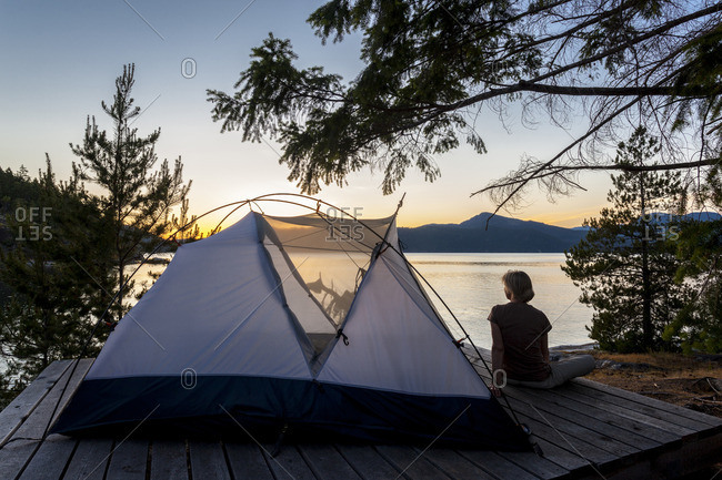 A camper relaxes on a platform next to her tent at dusk West Curme Island, Desolation Sound Marine Park, British Columbia, Canada Model Released