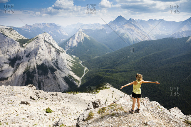 A young woman stands at the summit of the Sulphur Skyline Trail with a view of the Rocky Mountains Miette Hot springs, Jasper National Park, Alberta, Canada