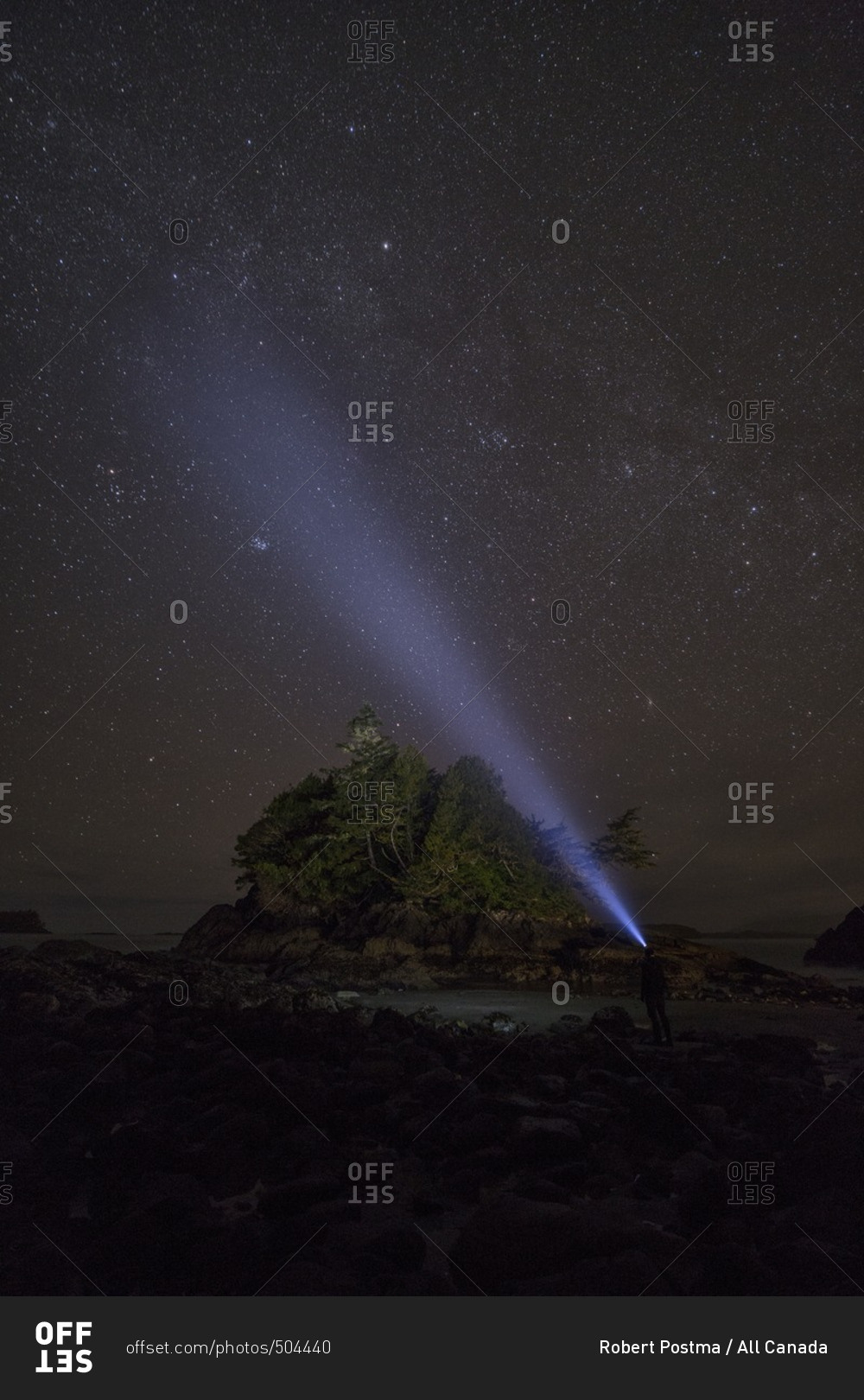 Man stands on the shore of the Pacific Ocean shining his headlamp into the night sky, Tofino, British Columbia, Canada, the Milky Way can be seen in the night sky