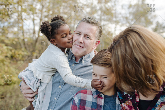 Little girl grabbing boys nose while standing with their parents