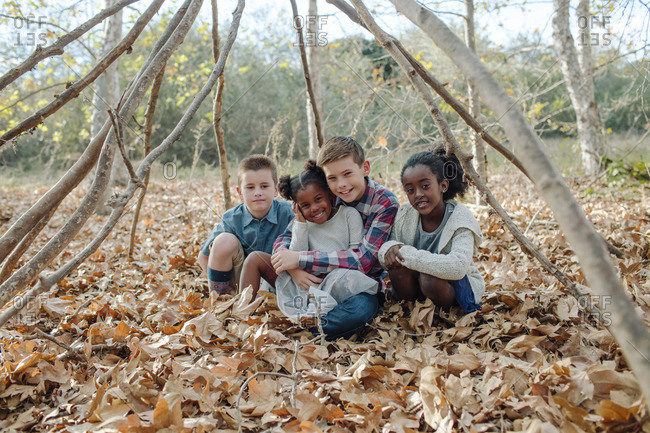 Children sitting in fallen leaves under a teepee
