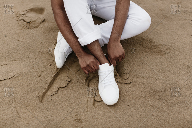 Man putting on white shoes on beach