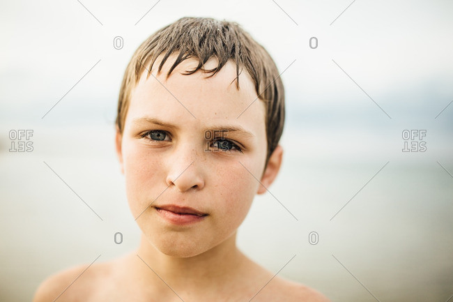 Boy with wet hair and sand on his face standing on a beach