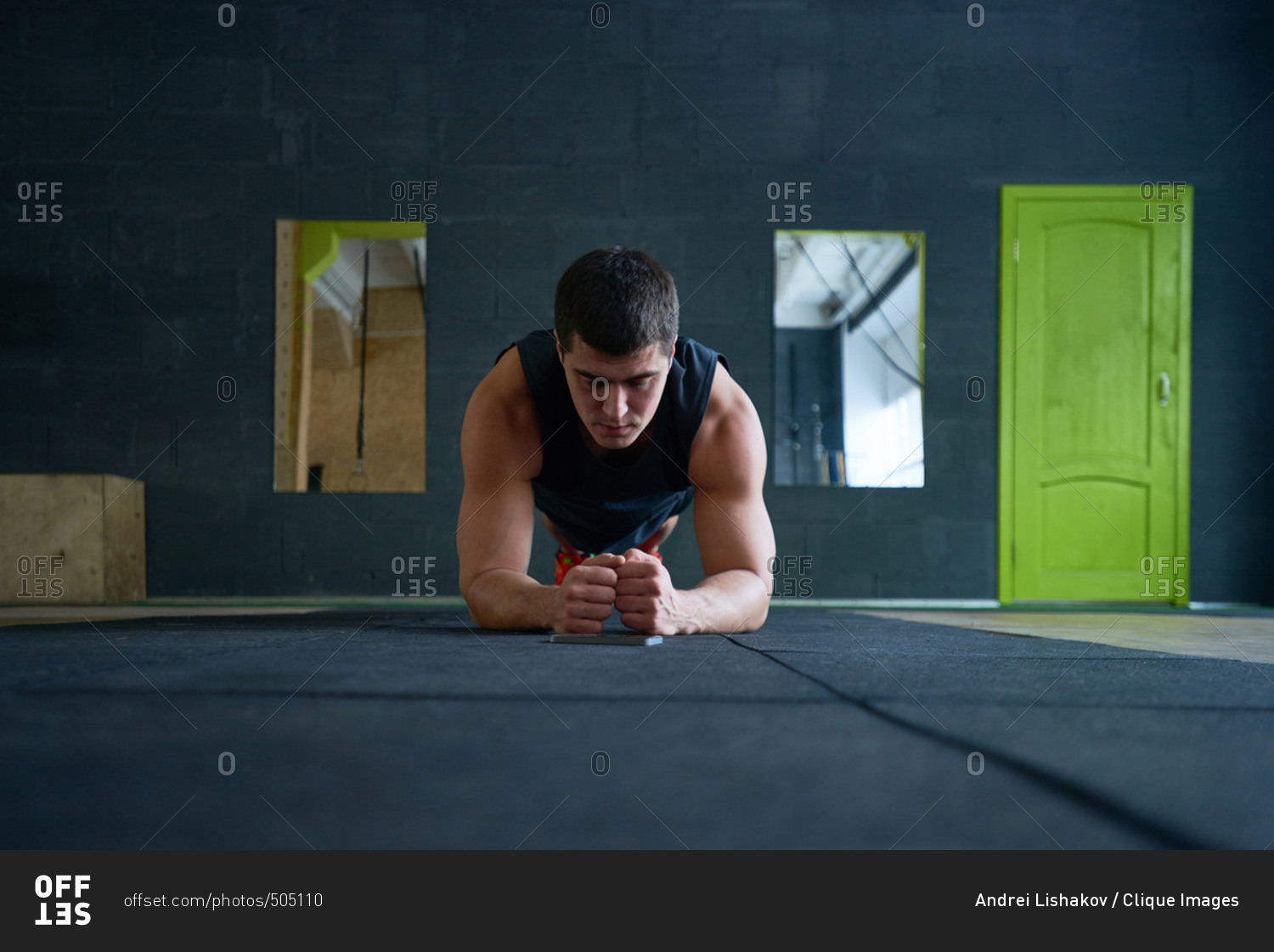 Young muscular dark-haired athlete in sportswear doing plank on mat while having bodyweight workout in fitness center