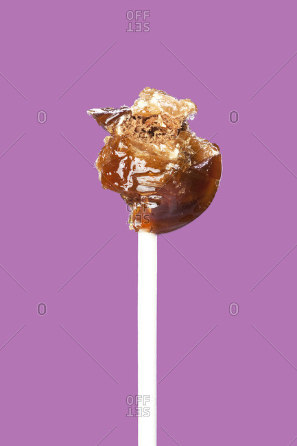 Close up of partially eaten lollipop in front of purple background