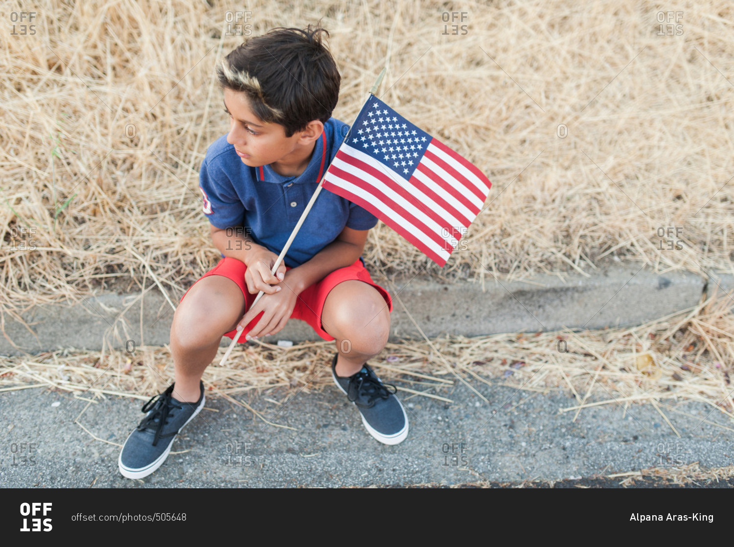 High angle view of a boy sitting on a curb holding American flag