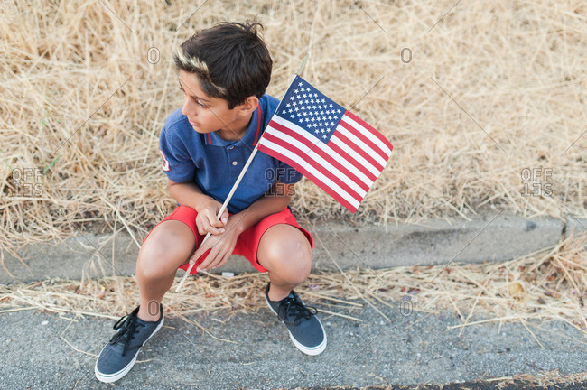 High angle view of a boy sitting on a curb holding American flag