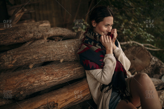 Woman is sitting on log pile and is looking joyfully in the distance